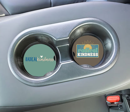 Two car cup holders with 'Radical Kindness' coasters inside a vehicle.